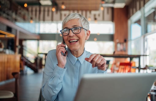 Vonage World Prime Image of woman on mobile phone sitting in a cafe in front of her laptop