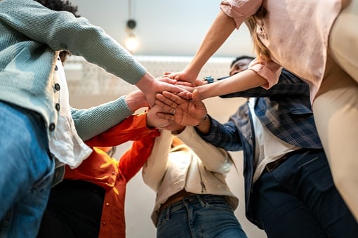 Coworkers joining hands together in the office, showing their unity and teamwork to achieve a common goal, promoting collaboration and support within the company