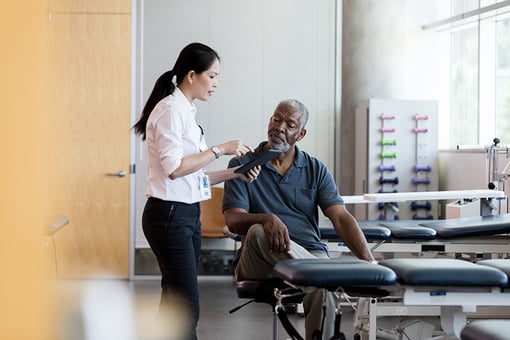 Attentive senior African American man listens as a female doctor shows him something on a digital tablet about his illness or condition.