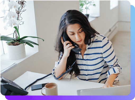 Woman on desk phone looking at her laptop and cell phones which ring at the same time