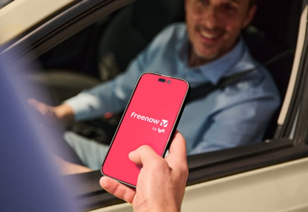 Image of person holding a mobile phone with the freenow app open, looking at a rideshare driver through the window