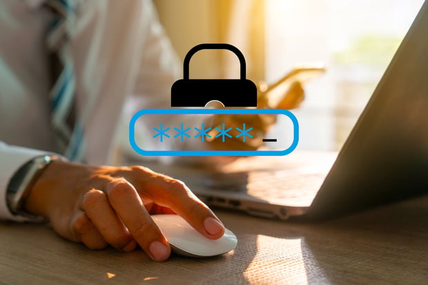 Close-up photo of a man holding a cell phone as he types in a password on his laptop. A lock icon is floating in the foreground, representing an account being broken into.