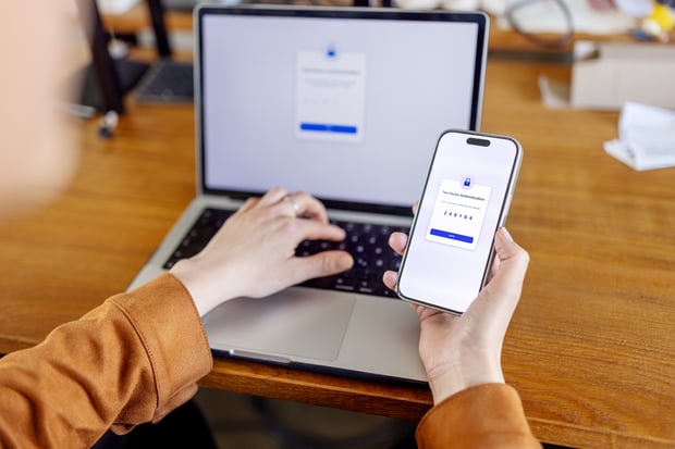 Close-up of female employee in tech office using two-factor authentication, entering smartphone code to access laptop securely.  Woman entering verification code from phone to laptop for secure login process.