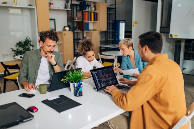  A man sitting at the same conference table in the office with a diverse group of people learn to code programs.