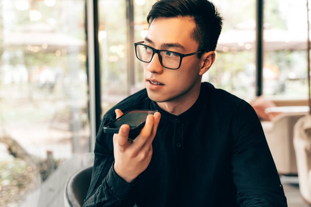 A man uses a mobile phone speak to an AI voice assistant. Reflects AI voice for customer engagement.