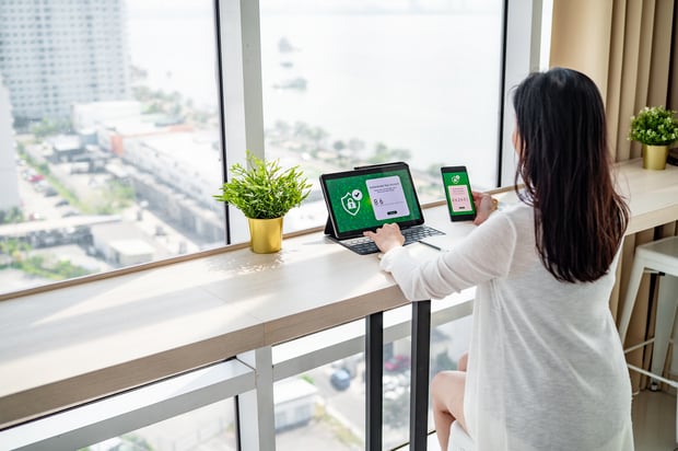 A woman working near window verifying login with 2FA on devices. Concept of passwordless authentication.
