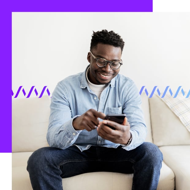 Photo of a smiling man at home texting or searching on his cell phone. In the background, a series of purple-blue wave forms runs across the frame.