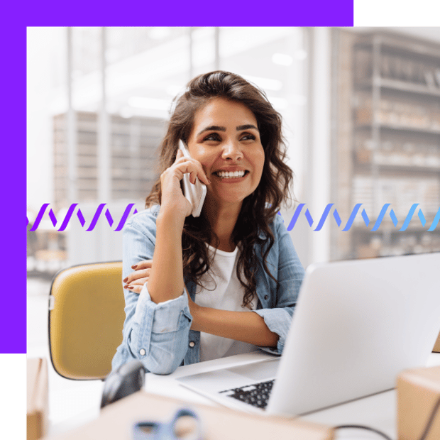 Photo of a smiling woman in an office setting. She is talking on her cell phone and sitting at a desk in front of her laptop. In the background, a series of small wave-like icons runs across the frame.