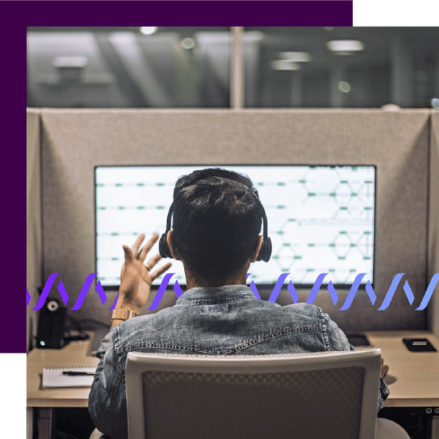 Photo of a call center agent taken from behind. Over his shoulder on the monitor screen can be seen an ongoing customer interaction. A series of small purple waveforms runs across the frame.
