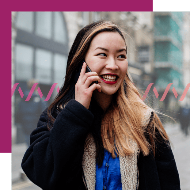 Photo of a smiling woman talking on her cell phone. She is in an outdoor city setting, with the background blurred.