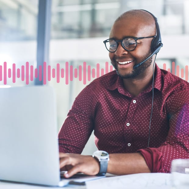 CC SEO Call Park Blog Header Photo of a smiling agent in an office typing on his laptop while speaking to a customer on his phone headset. In the background, a series of small pink vertical lines runs across the frame.