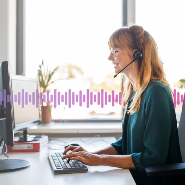 CC SEO Contact Center Blog Header Photo of a smiling woman working in an office. She is talking to a customer on her headset while typing notes into her computer. In the background, a series of small purple vertical lines runs across the frame.