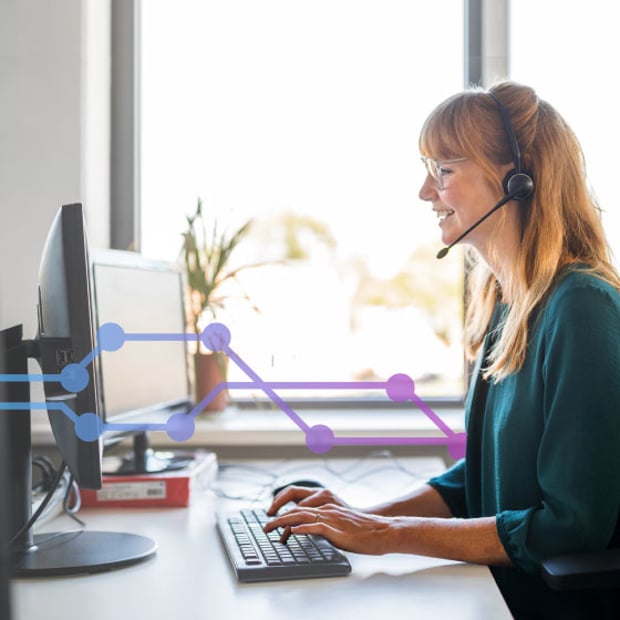 Photo of female contact center agent talking to a customer through her headset while typing notes in her computer.