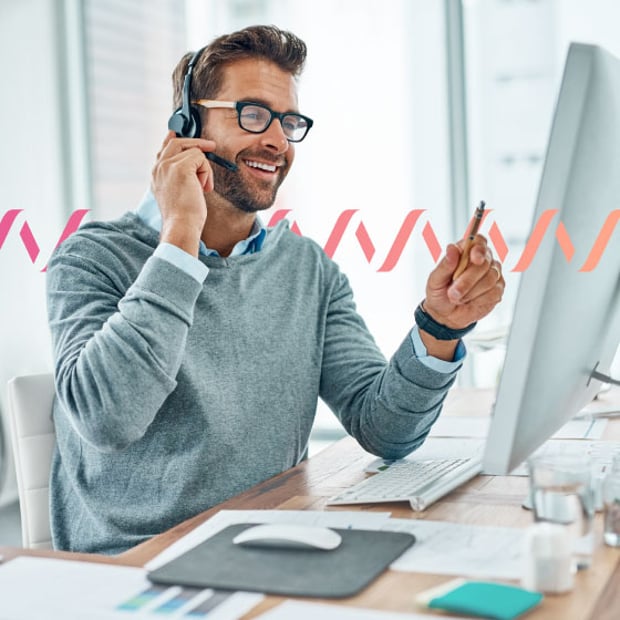 CC SEO Contact Center Compliance Blog Header Photo of a smiling contact center agent sitting in front of his computer and talking to a customer through his phone headset. In the background, a small gradient-pink waveform runs across the frame.