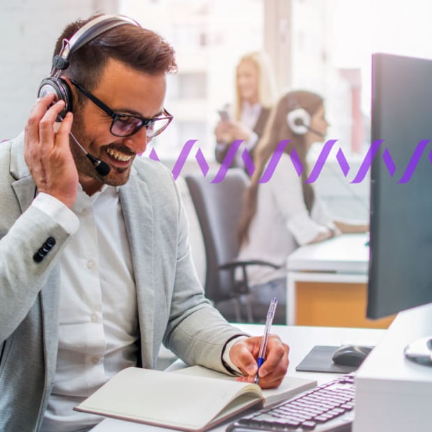 Photo of smiling call center agent writing notes in a pad while talking to a customer in his headset. In the background, a series of small purple waves runs across the frame, representing communication.