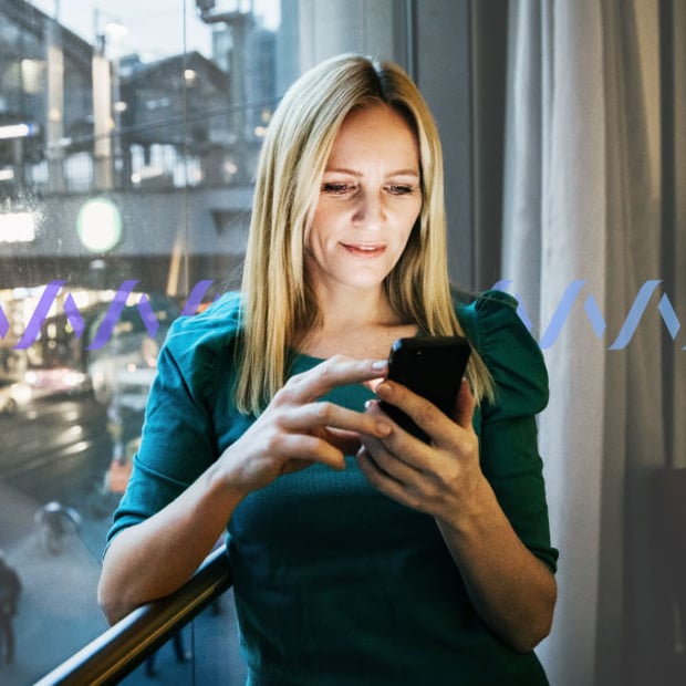SEO Customer Engagement Metrics Blog Header Photo of a woman standing by a window in a hotel room scrolling on her cell phone.