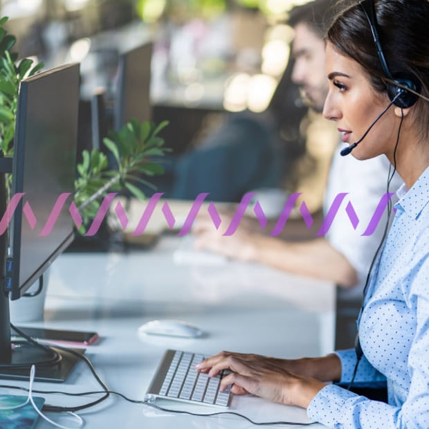 CC SEO Enterprise Contact Center Blog Header Photo of a row of contact center agents, seen from the side. They are talking to customers via their phone headsets while typing on their computers. In the background, a series of small purple waves runs across the frame.