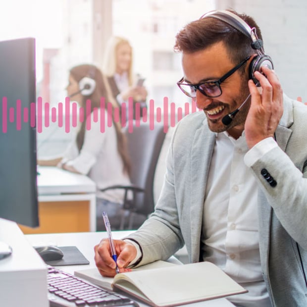 CC SEO Inbound Contact Center Blog Header Photo of a smiling contact center agent talking to a customer through his phone headset and taking notes. In the background, a series of small pink vertical lines runs across the frame.