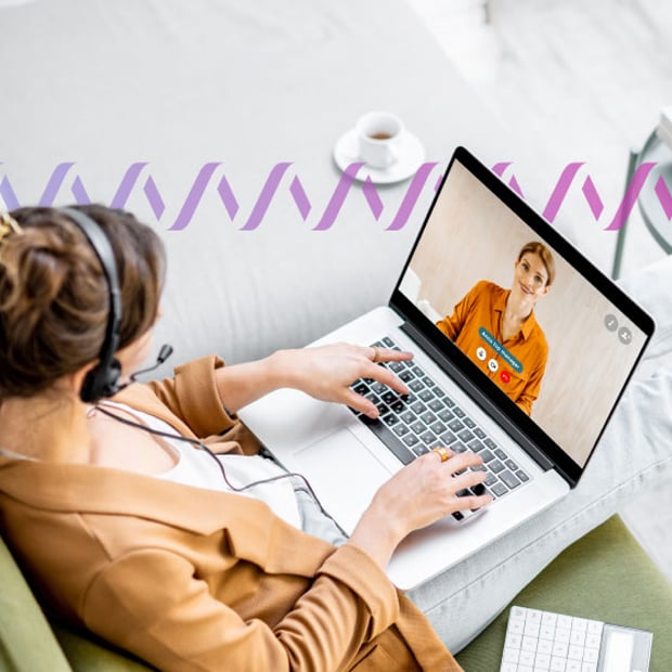 Photo of a woman sitting with her laptop in her lap and engaged in a video call. She is seen from above. You can see the person on the other side of the conversation in the computer screen. In the background, a series of small purple waves runs across the frame.