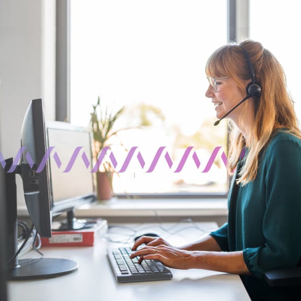 UC SEO CTI Blog Header Photo of a smiling woman in an office typing on her desktop computer while talking to someone on her phone headset. In the background, a series of small purple waves run across the frame, representing communication.