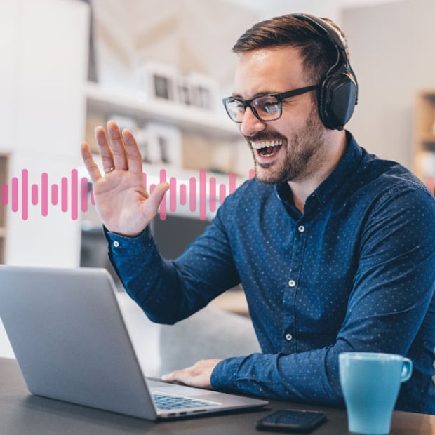 UC SEO VoIP Troubleshooting Blog Header Photo of a smiling employee in an office sitting in front of his laptop. He is talking on his headset and gesturing. In the background, a series of small pink vertical lines runs across the frame.
