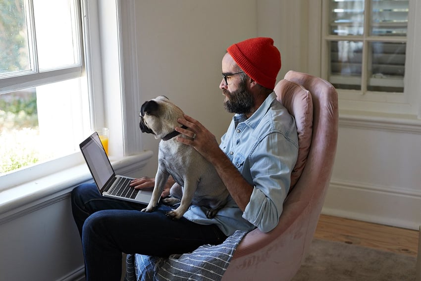 Man working from home with his dog on his lap while on his laptop