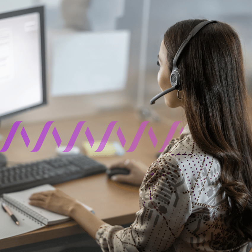 Photo of a female contact center agent wearing a headset and working at her computer.