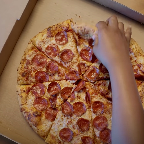 Hand reaching into pizza box grabbing a slice