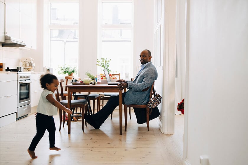 man in suit doing remote work with laptop from kitchen table man in suit doing remote work with laptop from kitchen table while child runs by