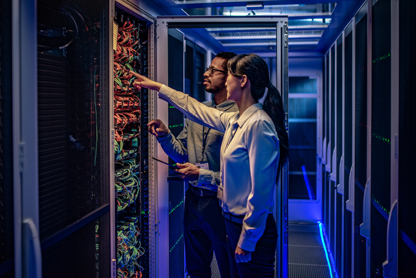 Photo of two IT team members in a server room discussing and troubleshooting the network system