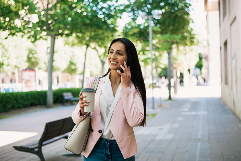 Photo of smiling woman outdoors away from the office on her cell phone.