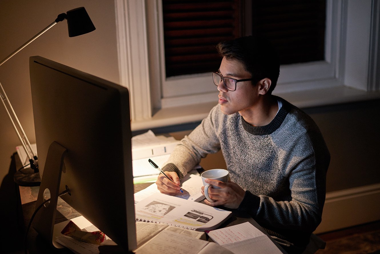 A male student sitting at a desk taking a class from home on his computer